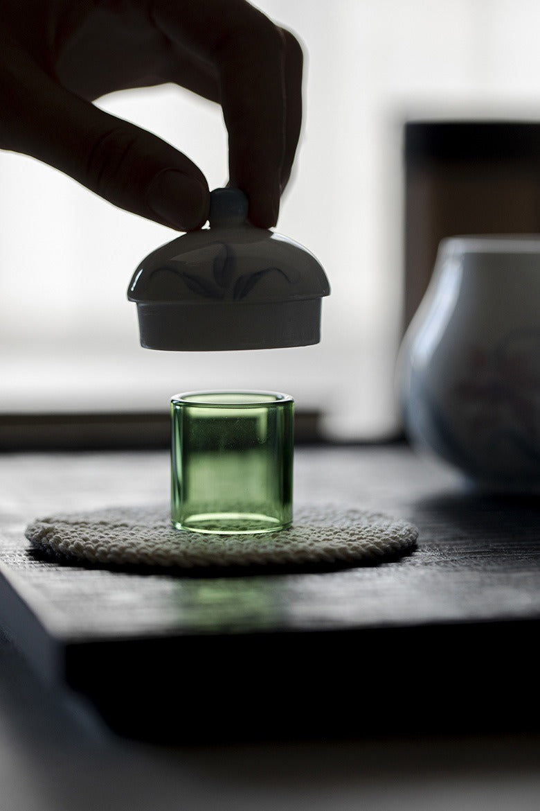 Green glass holder for lid on a textured coaster, blurred background