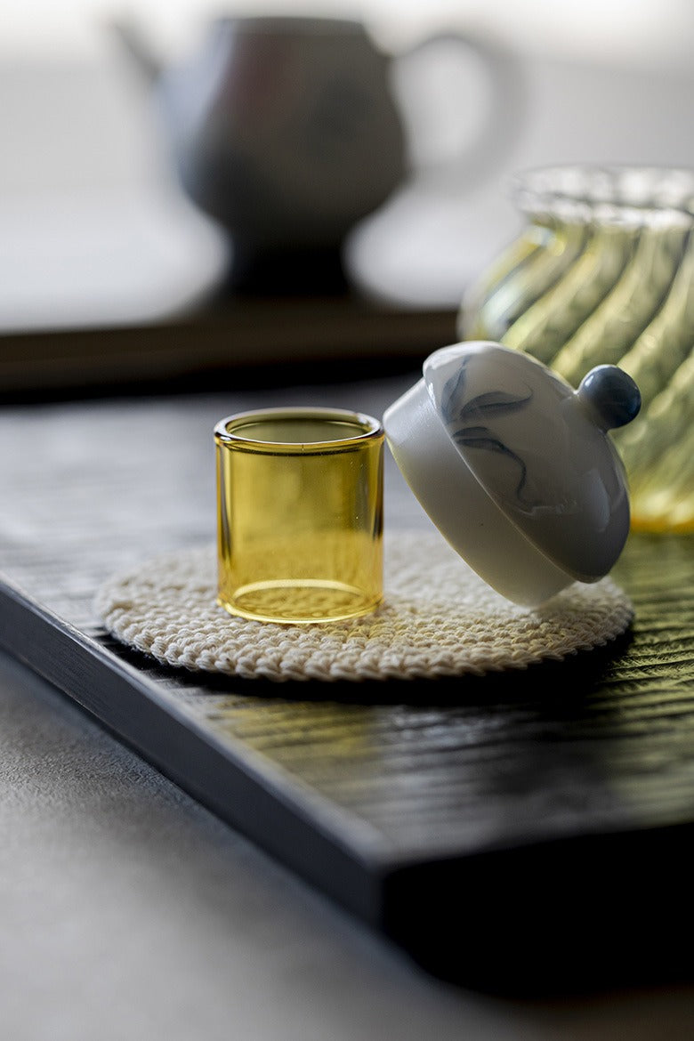 Yellow glass lid holder with white lid on a woven coaster, blurred background